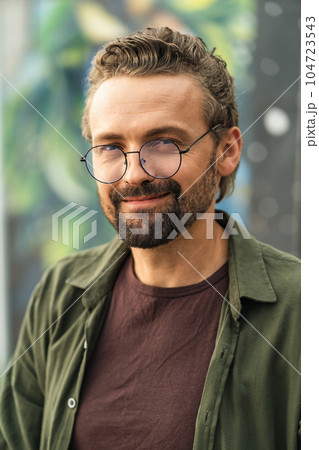 Handsome individual wearing glasses, situated outdoors against a graffiti-covered background. With a stylish and confident appearance, the subject exudes a modern and trendy vibe. . High quality photo 104723543