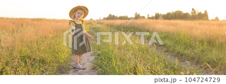 A little blonde girl in a straw hat walks in a field with a bouquet of daisies. The concept of walking in nature, freedom and an eco-friendly lifestyle. 104724729