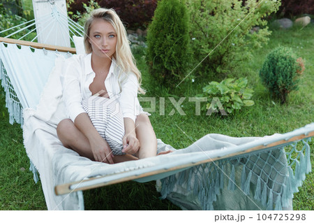A beautiful blonde woman is lying on a hammock in her summer cottage. The concept of life in the country and summer holidays. 104725298