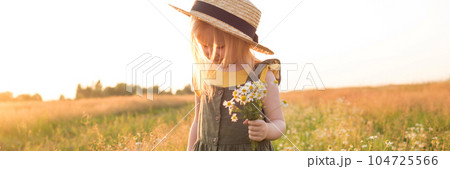 A little blonde girl in a straw hat walks in a field with a bouquet of daisies. The concept of walking in nature, freedom and an eco-friendly lifestyle. 104725566