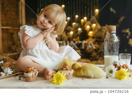 A little girl is sitting on the Easter table and playing with cute fluffy ducklings. The concept of celebrating happy Easter. A little girl is sitting on the Easter table and playing with cute fluffy ducklings. The concept of celebrating happy Easter. 104726216