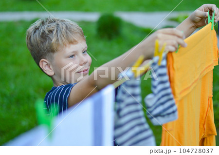 A happy caucasian 9 years boy helps her mother to hang up clothes. Development of fine motor skills through household activities. Selective focus. 104728037