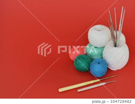 A closeup shot of red, purple, and blue knitting yarns and crochet hooks 104728482