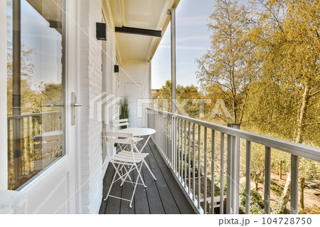 a balcony with chairs and trees in the background on a sunny day, taken from an open window looking outside 104728750