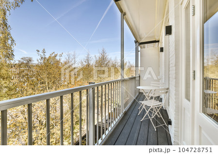 a balcony with chairs and trees in the background on a sunny day, taken from an open window looking outside 104728751