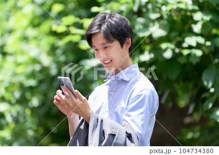 屋外にてスマホを見て喜ぶ若い男性 屋外にてスマホを見て喜ぶ若い男性 104734380