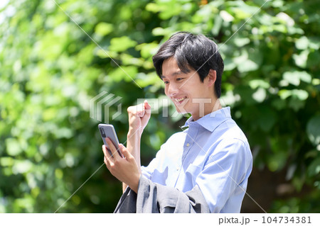 屋外にてスマホの画面を見てガッツポーズをとる若い男性 屋外にてスマホの画面を見てガッツポーズをとる若い男性 104734381