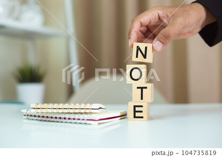 Word NOTE on wood cubes, Hand holding wooden block stacking with note alphabet and notebooks nearby 104735819