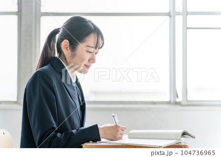 学校の教室で数学の教科書・参考書を見ながら勉強する女子高校生・中学生の生徒 104736965