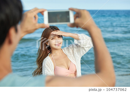 young couple taking pictures on their smartphones on the beach 104737062