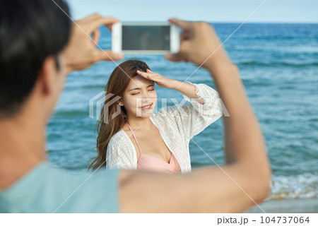 young couple taking pictures on their smartphones on the beach 104737064
