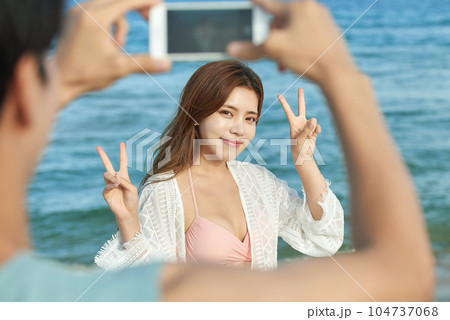 young couple taking pictures on their smartphones on the beach 104737068