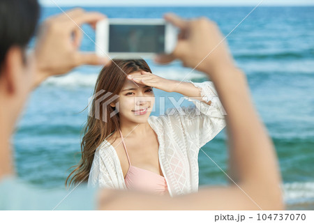 young couple taking pictures on their smartphones on the beach 104737070