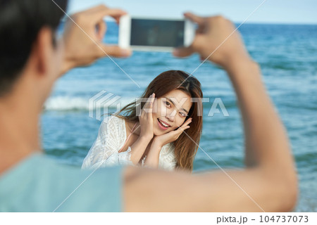 young couple taking pictures on their smartphones on the beach 104737073