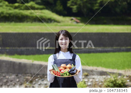 畑の前で採れたての野菜をもつ農家の女性 104738345