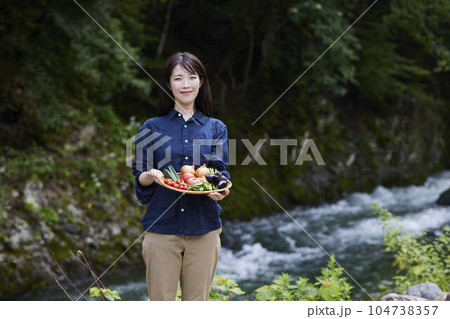 川の前で採れたての野菜をもつ農家の日本人女性 104738357
