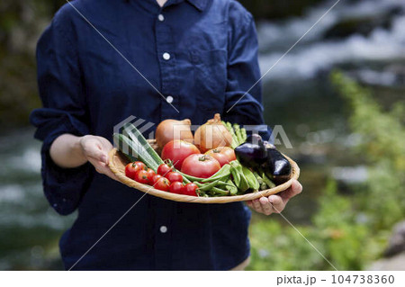 川の前で採れたての野菜をもつ農家の日本人女性 川の前で採れたての野菜をもつ農家の日本人女性 104738360