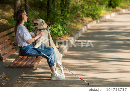 Blind young woman cuddling with guide dog while sitting on a bench. Blind young woman cuddling with guide dog while sitting on a bench. 104738757