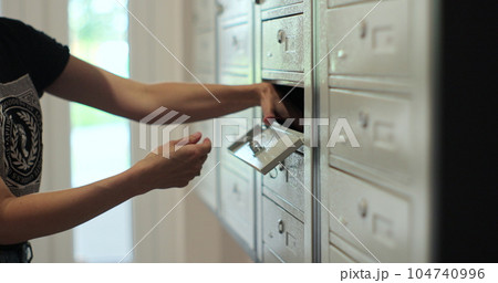 Woman is opening her mailbox inside a cluster of mailboxes for her apartment. Mail shipping concept. Woman is opening her mailbox inside a cluster of mailboxes for her apartment. Mail shipping concept. 104740996
