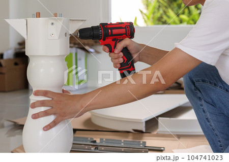 man assembling white table furniture at home using cordless screwdriver man assembling white table furniture at home using cordless screwdriver 104741023