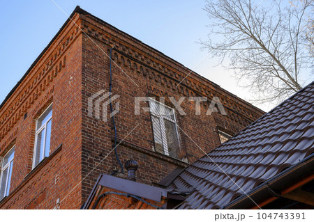 The geometry of an old brick building, roof tiles and branches of a spring tree against the sky The geometry of an old brick building, roof tiles and branches of a spring tree against the sky 104743391