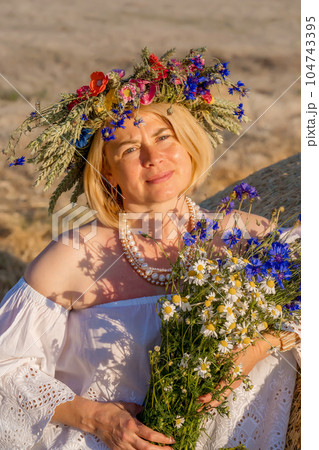 Beautiful woman in summer dress enjoying summer in field. Beautiful young lady in wildflower wreath. Cute girl in a flowers wreath on the nature. 104743395