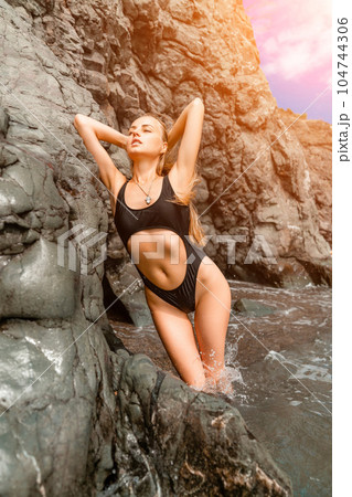 Woman swimsuit sea. Attractive blonde woman in a black swimsuit enjoying the sea air on the seashore around the rocks. Travel and vacation concept. Woman swimsuit sea. Attractive blonde woman in a black swimsuit enjoying the sea air on the seashore around the rocks. Travel and vacation concept. 104744306