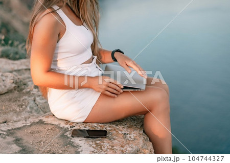 Freelance women sea working on the computer. Good looking middle aged woman typing on a laptop keyboard outdoors with a beautiful sea view. The concept of remote work. Freelance women sea working on the computer. Good looking middle aged woman typing on a laptop keyboard outdoors with a beautiful sea view. The concept of remote work. 104744327