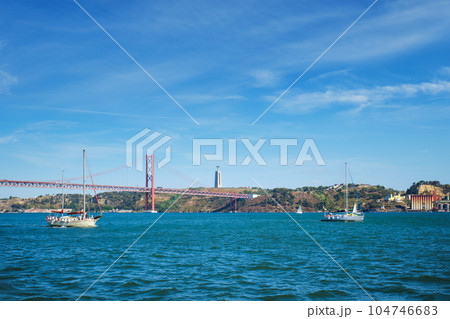 View of 25 de Abril Bridge famous tourist landmark over Tagus river, Christ the King monument and a tourist yacht boat. Lisbon, Portugal 104746683