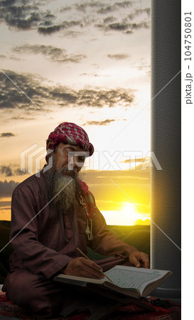 Muslim man with a beard wearing keffiyeh with agal sitting and reading the Quran on the prayer rug Muslim man with a beard wearing keffiyeh with agal sitting and reading the Quran on the prayer rug 104750801