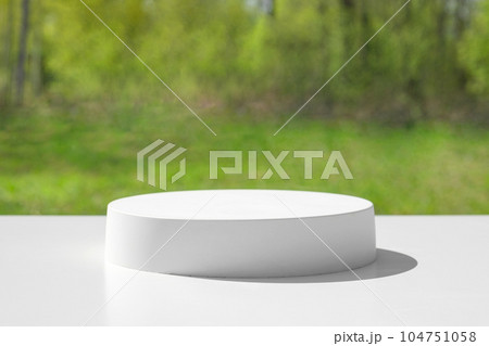 Podium for presentation. Blurred green grass background. Abstract geometrical form. Cylinder stone sphere. Shadow. Scene to show products. Showcase, display case. Trendy sunlight. Front view. 3D 104751058