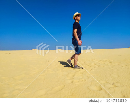 Young man in straw hat and dark shorts walking in desert Young man in straw hat and dark shorts walking in desert 104751859
