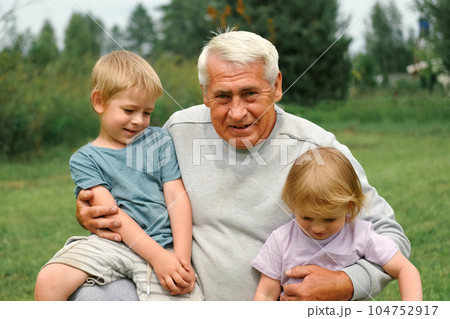 Grandfather and grandchildren have fun during walk In Park. Happy family time. Old man grandpa hugging children boy and girl. Summer day. Smiling Senior male spending time with his grandkids together Grandfather and grandchildren have fun during walk In Park. Happy family time. Old man grandpa hugging children boy and girl. Summer day. Smiling Senior male spending time with his grandkids together 104752917