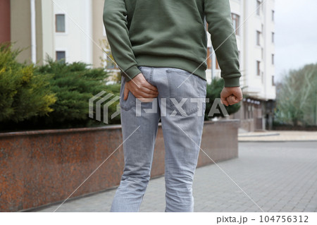 Man suffering from hemorrhoid pain outdoors, closeup 104756312