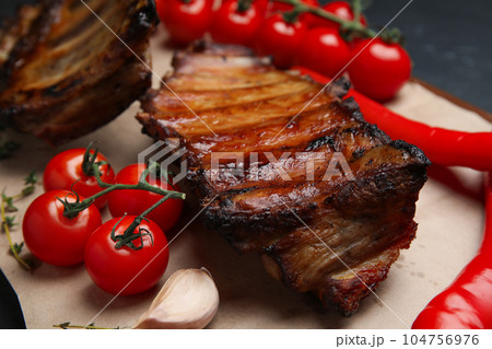 Tasty grilled ribs with tomatoes and peppers on table, closeup 104756976