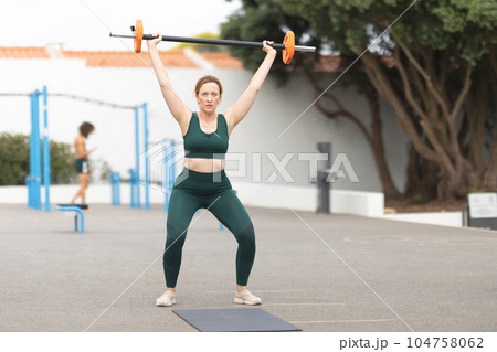 Adult sportive woman lifting a dumbbell on the outdoors sports ground 104758062