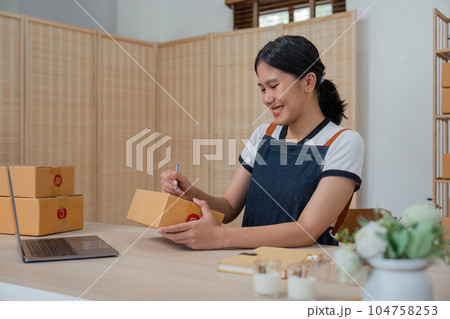 Woman runs an ecommerce business is writing a list of customers on box before shipping to customer, Concept of selling products online 104758253