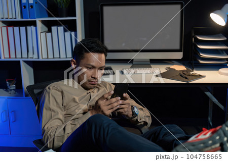 Overworked young Asian office employee working on laptop computer overtime in office at night 104758665