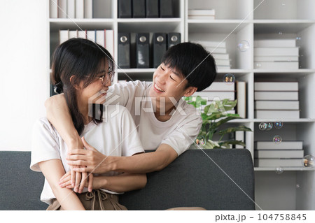 Smiling young couple embracing at office. Smiling man embracing from behind her happy girlfriend Smiling young couple embracing at office. Smiling man embracing from behind her happy girlfriend 104758845
