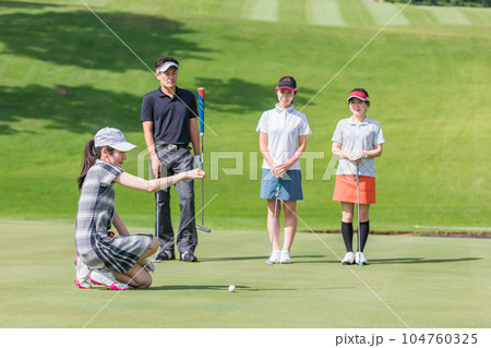 ゴルフ場のグリーンでゴルフをするゴルファーの男女(パター) 104760325
