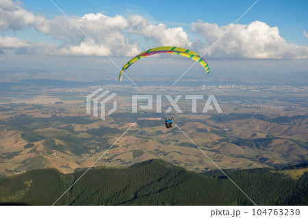 colored Paraglider flying over mountain valley on a sunny clear day 104763230