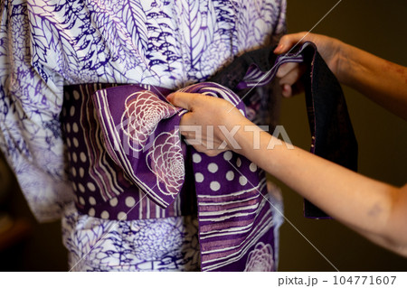 白地に型染の浴衣を着た女性に帯を結んでいるところ 白地に型染の浴衣を着た女性に帯を結んでいるところ 104771607