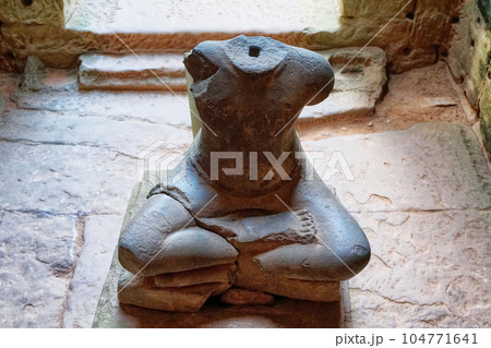 Image showcasing a damaged sculptural representation of Buddha in an ancient Cambodian temple, with notable decapitation, indicative of vandalism. 104771641