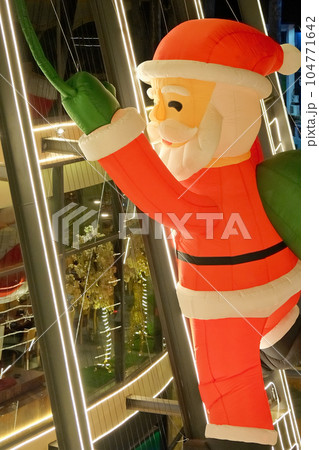 Image depicting a sizable inflatable Santa Claus figure attached to a building wall, appearing as if it's climbing. Image depicting a sizable inflatable Santa Claus figure attached to a building wall, appearing as if it's climbing. 104771642