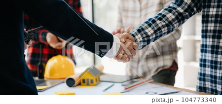 Three colleagues discussing data working and tablet, laptop with on on architectural project at construction site at desk in office.. Three colleagues discussing data working and tablet, laptop with on on architectural project at construction site at desk in office.. 104773340