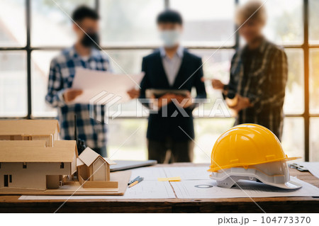 Engineer desk with object paper and tablet with blurry engineer teamwork hardworking to consults about their building project.in office Engineer desk with object paper and tablet with blurry engineer teamwork hardworking to consults about their building project.in office 104773370