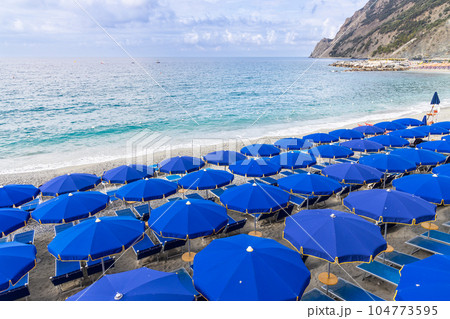 Colorful umbrellas and chairs along the beach front of Monterosso coast, one of the village in Cinque Terre, Italy 104773595