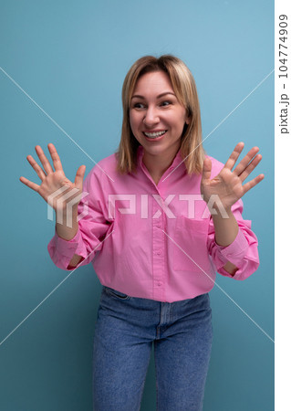 young pleasant stylish blond woman is dressed in a pink shirt and jeans gesturing with her hands 104774909