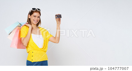 Happy young woman holding shopping bags and showing credit card isolated on white background. 104777007