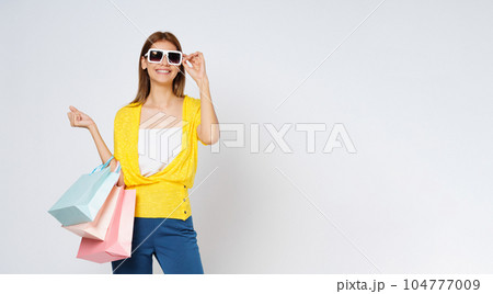Happy young woman wearing sunglasses and holding  shopping bags isolated on white background. 104777009